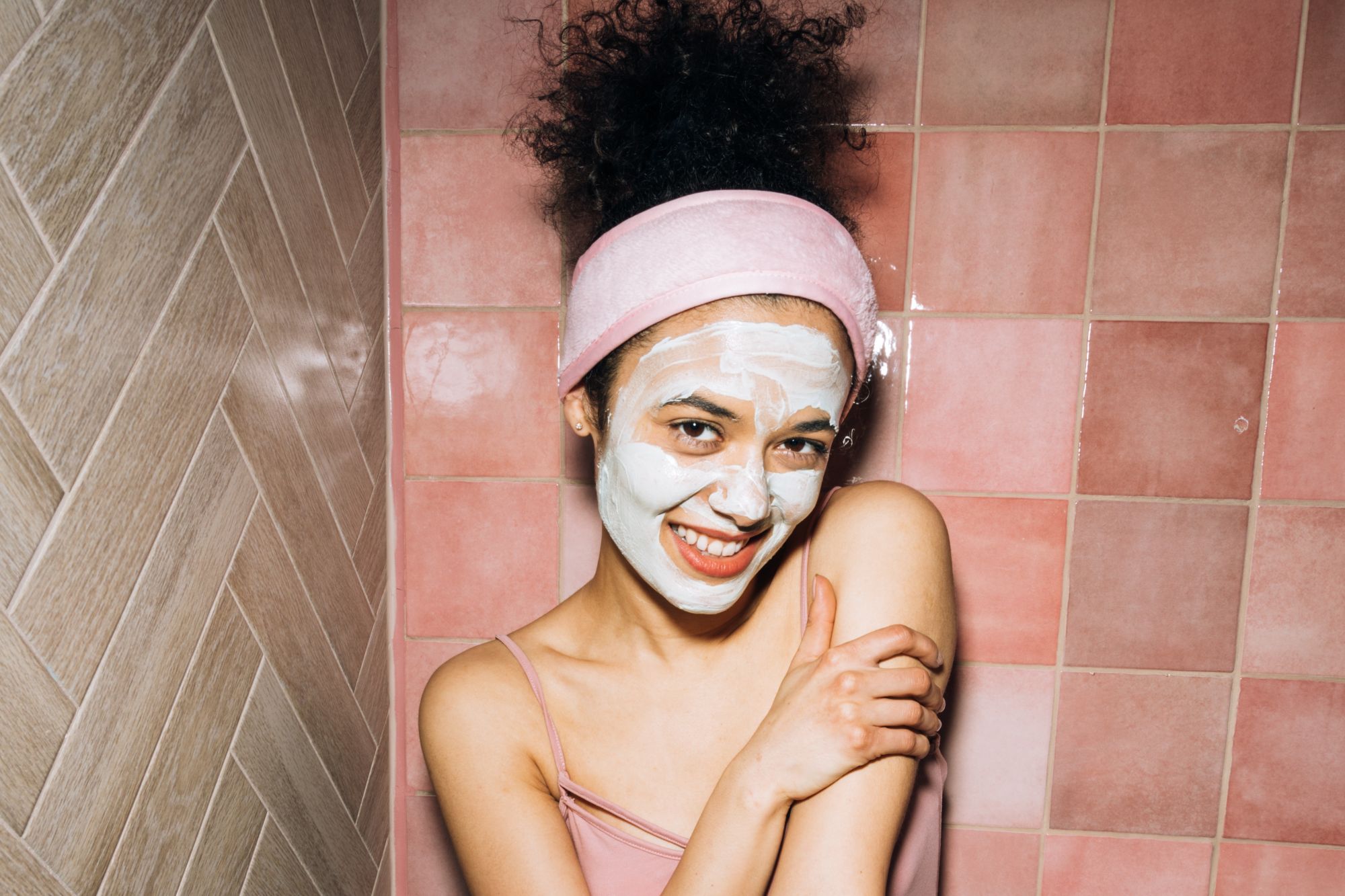 woman of colour in a pink shower with a face mask on and pink headband.