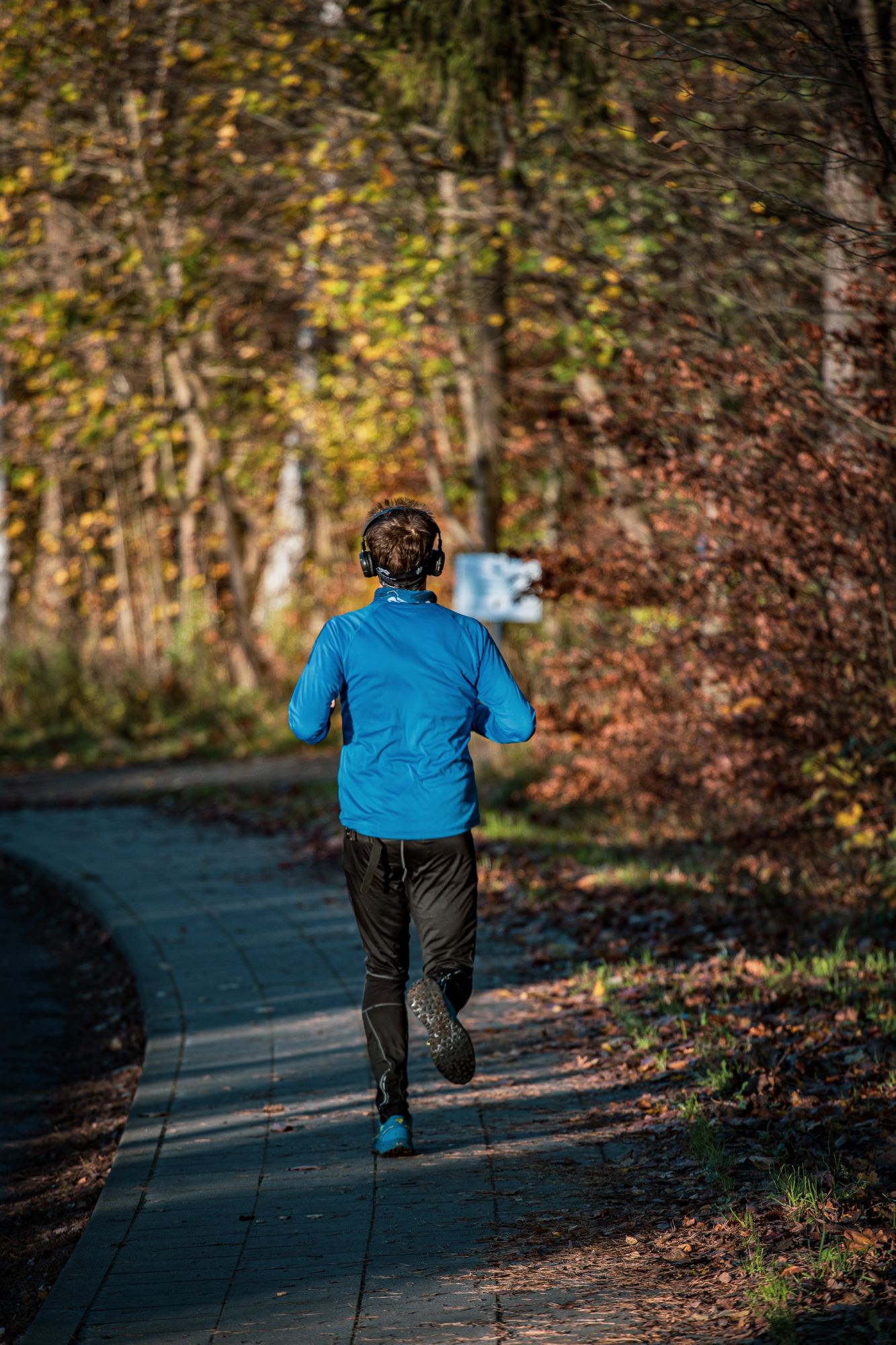 man running with headphones on a autumn coloured tree path.